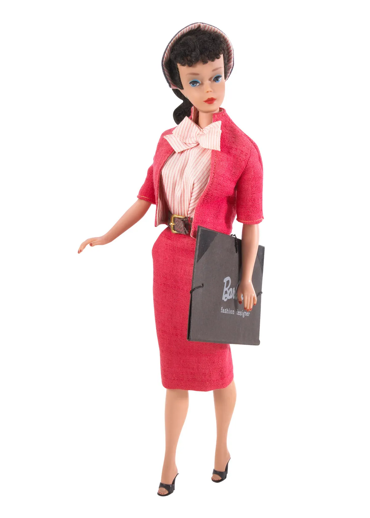 Fashion Designer Barbie, released in 1960. The doll wears a red dress set and a black tote bag that displays her title